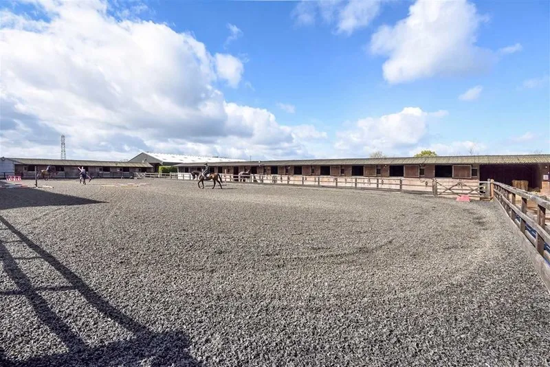 The large outdoor arena under a blue sky, with stables beyond